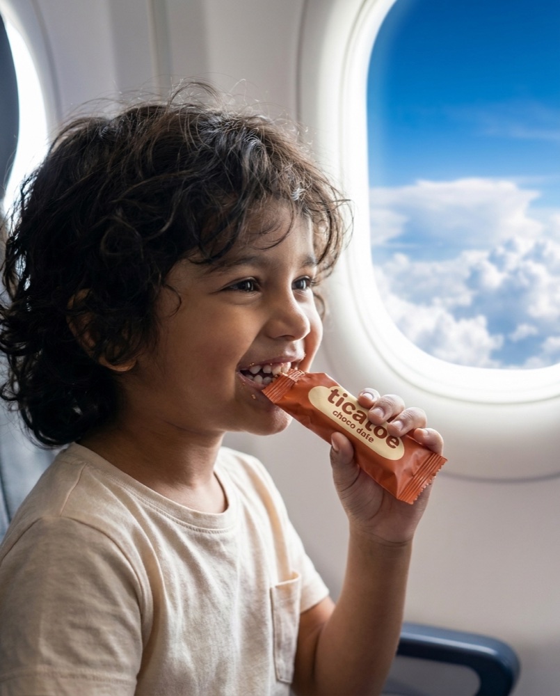 Kid on a flight with a ticatoe bar, clouds out the window